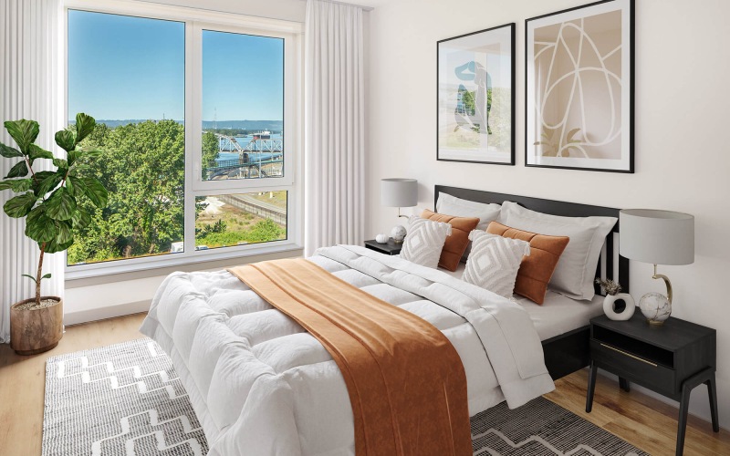 Spacious bedroom with a white bed, orange accents, abstract artwork, and a large window offering a scenic view